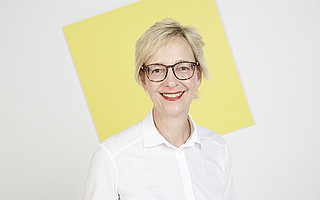 Portrait von Christine Regitz auf weißem Hintergrund mit gelber Kachel